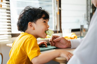 Büyükbaba torununa sabah kahvaltısını yemek odasında yedirir..