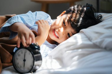 Küçük çocuk rahat bir yatakta uzanır, gündüz uyanır ve çalar saatin yanında uyur..