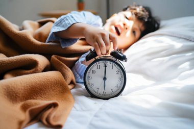 Küçük çocuk antika çalar saati çalarken yatağa uzanıyor..