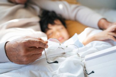 Torunuyla gündüz uyurken büyükbabanın elindeki gözlüklerin kırpılmış görüntüsü..