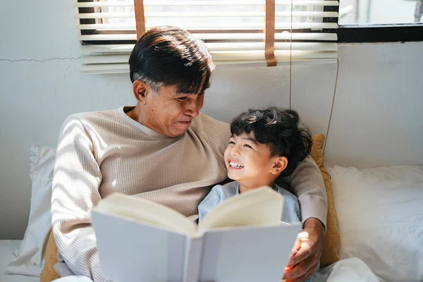 Old man with gray hair tell the bedtime story for his grandson for daytime sleep.