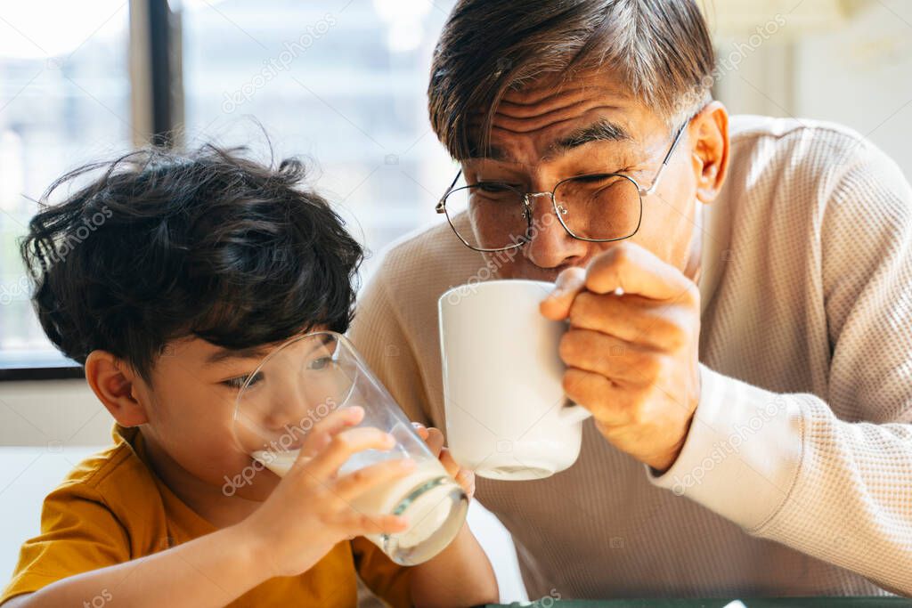 Little boy and his grandpa drinking the beverage together, he drink the milk while his grandpa drink the coffee in the morning.