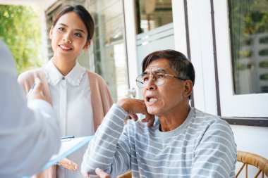 Gri saçlı yaşlı bir adam ve kızı ev ziyareti sırasında doktora durumundan bahsediyorlar..
