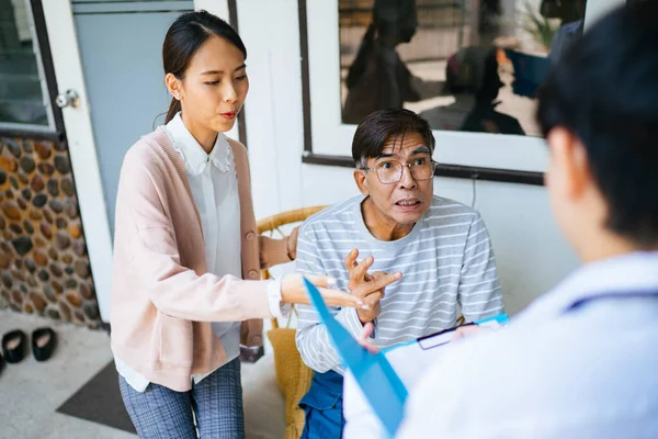 Old man with gray hair and his daughter tell the doctor about his condition during home visit.