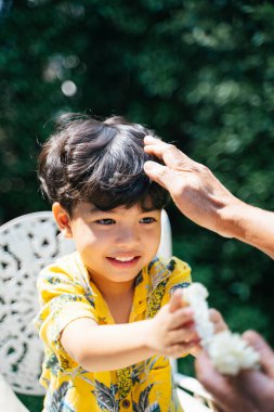 Küçük çocuk dedesine yasemin çelengi verir sonra da dedesinin elini döker, dedesinin başını nazikçe ovuşturur..