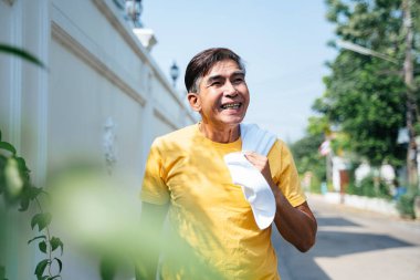 Sarı tişörtlü yaşlı adam yazın beyaz havluyla koşuyor..