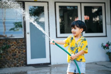 Küçük çocuk, geleneksel Tayland günü Songkran 'daki evinde su tabancası ve lastik tüple suya su sıçrattı..