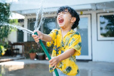 Küçük çocuk, geleneksel Tayland günü Songkran 'daki evinde su tabancası ve lastik tüple suya su sıçrattı..