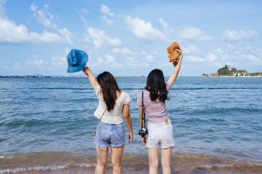 İki kız kumsalda eğlenirken denizde gezerler, şapkalarını havaya kaldırırlar..