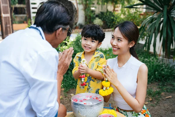 Mother teach her son to pay respect to grandpa by press the hands together at the chest with jasmine garland as a traditional activity in Thai family day.