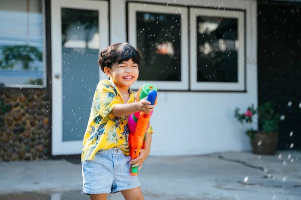 Küçük çocuk, geleneksel Tayland günü Songkran 'daki evinde su tabancası ve lastik tüple suya su sıçrattı..
