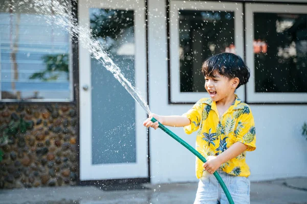Küçük çocuk, geleneksel Tayland günü Songkran 'daki evinde su tabancası ve lastik tüple suya su sıçrattı..