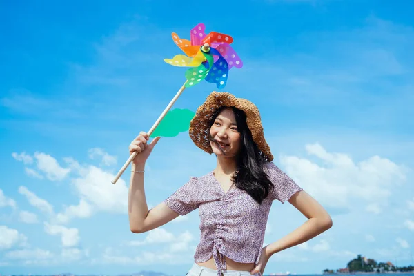 幸せなかわいいです女の子身に着けている茶色の帽子ホールドザカラフルな風車で風の日下の青空と白い雲で夏 — ストック写真