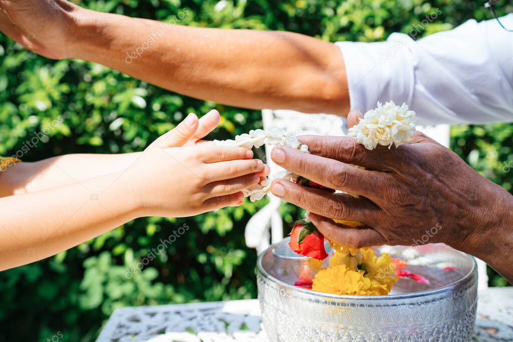 Cropped image of old man's hand take the jasmine garland from his grandchild over the table with silver bowl.