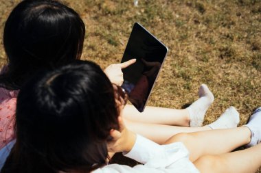 İki kız yaz güneşinde ve rüzgarda sahada oturup e-kitap okuyorlar..