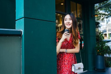 Kırmızı elbiseli neşeli Asyalı kadın açık kafede bir fincan kahve tutuyor..