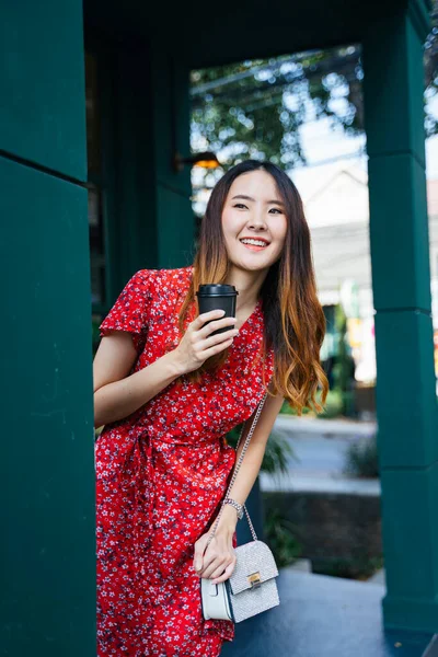 陽気若いですアジア人女性上の赤いドレス保持Aカップのコーヒーでカフェ屋外 — ストック写真