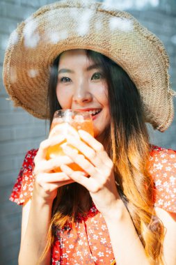 Kırmızı elbiseli neşeli Asyalı kadın hasır şapkalı tatlı kafeteryasında buzlu içecek içiyor..