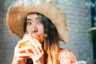 Kırmızı elbiseli neşeli Asyalı kadın hasır şapkalı tatlı kafeteryasında buzlu içecek içiyor..