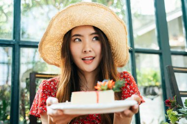 Kırmızı elbiseli, elinde peynirli kek tabağı olan Asyalı genç bir kadın portresi. Tatlı sever..