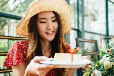 Kırmızı elbiseli, elinde peynirli kek tabağı olan Asyalı genç bir kadın portresi. Tatlı sever..