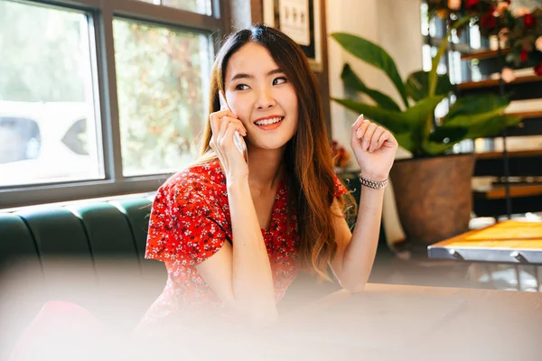 Kırmızı elbiseli genç Asyalı kadın kahve dükkanında telefonla konuşuyor..