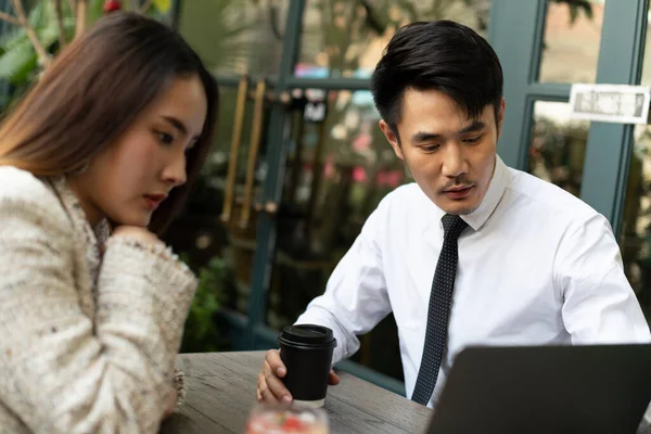 Young asian business people working together at coffee shop looking at presentation on laptop.