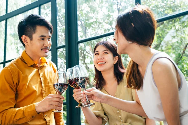 Group of cheerful friends drinking and toasting red wine. Asian thai people having fun together at restaurant.