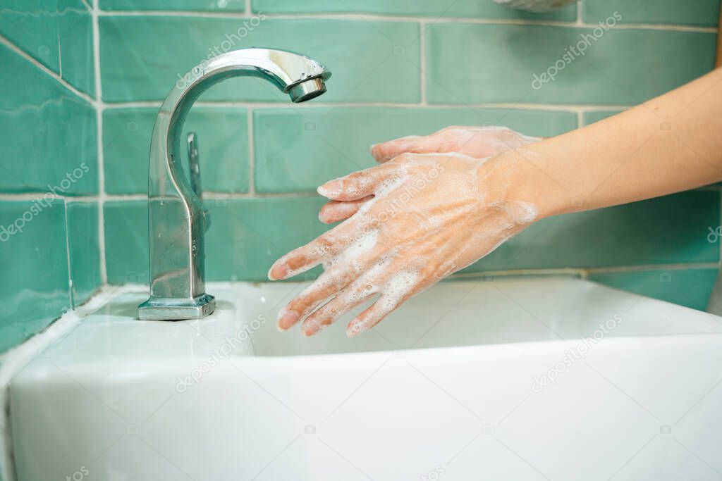 Hygiene concept. Washing hands with soap under the faucet with water in green bathroom toilet. Washing of hands with soap under running water.