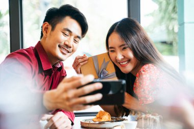 Kırmızı elbiseli Asain Thai çifti birbirlerini şaşırtırlar. Sevgililer gününde sevgilisine hediye paketi getiren bir adam. Romantik çift, anılarını fotoğrafa kaydetmek için akıllı telefonuyla selfie çekiyor..