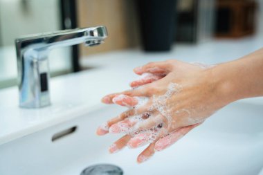 Kadınlar banyo lavabosunda su ve sabunla el yıkıyorlar. Eller kadın umumi tuvalette musluk ya da beyaz lavabo ile su musluğu açıyor.