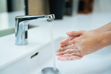 Kadınlar banyo lavabosunda su ve sabunla el yıkıyorlar. Eller kadın umumi tuvalette musluk ya da beyaz lavabo ile su musluğu açıyor.