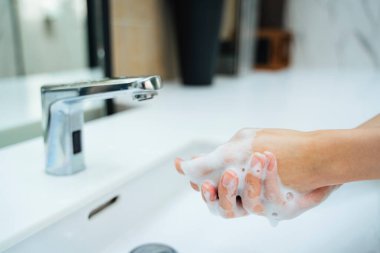 Kadınlar banyo lavabosunda su ve sabunla el yıkıyorlar. Eller kadın umumi tuvalette musluk ya da beyaz lavabo ile su musluğu açıyor.