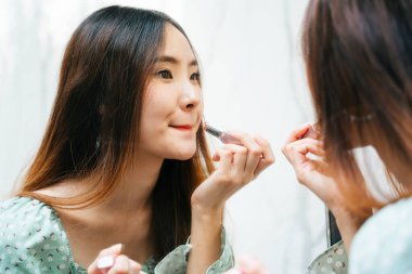 Asyalı Taylandlı kadının yüzünü kapat. Uzun saçlı. Aynanın karşısına ruj sürüyor..