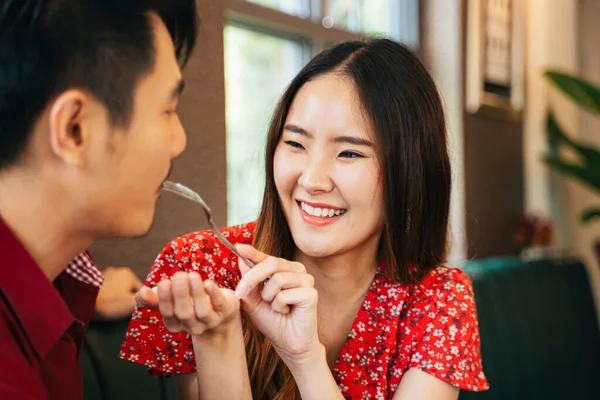 Beautiful asian woman feeding dessert cake with fork to her boyfriend.