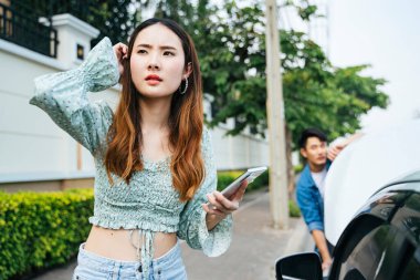 Asyalı bir kadın bozuk bir arabanın yanında duruyor ve yardım için cep telefonu kullanıyor.. 