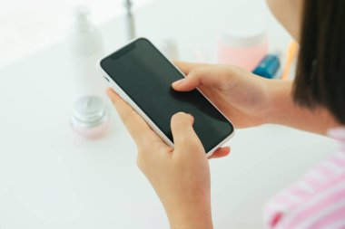 Genç ve güzel Asyalı Taylandlı siyah kısa saçlı kadın tuvalette akıllı telefon kullanıyor..