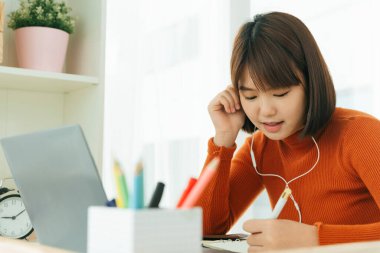 Asyalı genç, güzel, kısa saçlı, kısa saçlı, siyah bir kadın. İnternetten öğreniyor ve kulaklık takıyor..