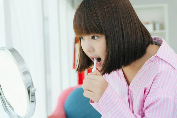 Genç ve güzel Asyalı Taylandlı kısa saçlı kadın tuvalette diş fırçasıyla dişlerini fırçalıyor..