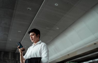 Havaalanından ayrılmadan önce akıllı telefondan taksi çağıran beyaz tişörtlü Asyalı bir iş adamı. Akıllı Asyalı işadamı akıllı telefondan konuşuyor..