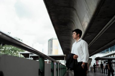 Beyaz tişörtlü, olgun Asyalı iş adamı tek başına yolda dikilip yola bakıyor..