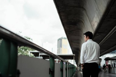 Beyaz tişörtlü, Asyalı bir iş adamı yolda yürürken yola bakıyor..