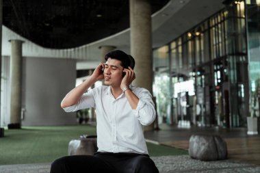 Beyaz tişörtlü olgun Asyalı iş adamı kendini mutlu hissediyor. Kablosuz kulaklıktan müziğin tadını çıkarıyor. Kulağıma müzik geliyor..