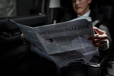 Asyalı işadamı arabada gazete okuyor ve en son borsa raporunu inceliyor., 