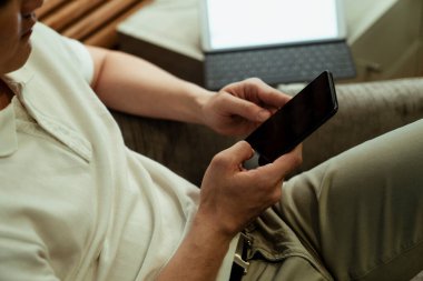 Kanepede oturmuş akıllı telefon kullanan Asyalı adamın elini kapat..