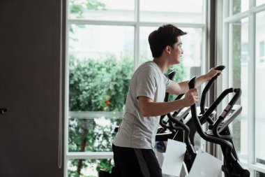 Spor salonunda çalışan günlük giysili genç Asyalı adam koşu makinesi kullanıyor. Evde egzersiz yapmak..