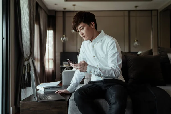 Azjata Białym Kołnierzyku Trzyma Smartfona Sprawdzając Harmonogram Patrząc Laptopa Siedzącego — Zdjęcie stockowe