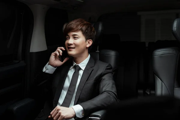 Smart asian businessman on black suit talking on the phone in luxury car.