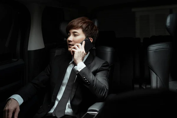 Smart asian businessman on black suit talking on the phone in luxury car.