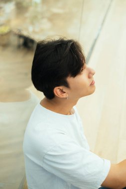 Beyaz tişörtlü, barikata yaslanmış genç bir adamın yüksek açılı fotoğrafı..